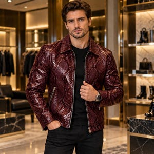 May include: A dark burgundy jacket with a textured snakeskin pattern, featuring a classic collar, long sleeves, and a silver-toned front zip fastening. The garment is worn over a plain black shirt and paired with black trousers.