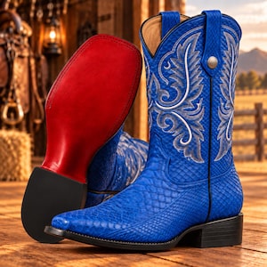 Op de afbeelding: Een paar felblauwe cowboylaarzen met een gestructureerd slangenleerpatroon, een vierkante neus en ingewikkeld wit borduurwerk op de schacht. De ene laars staat rechtop, terwijl de andere zo is geplaatst dat de gladde, rode zool zichtbaar is.