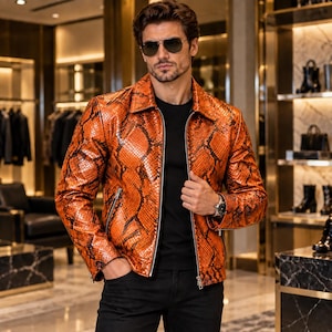 May include: A vibrant orange and black snakeskin-patterned leather jacket with a classic collar, long sleeves, and a silver-toned front zip fastening. The jacket is worn over a plain black t-shirt, paired with black trousers and a silver wristwatch.