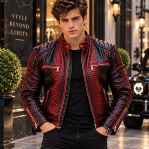 Op de afbeelding: Een rood en zwart leren jack met slangenleertextuur, voorzien van een opstaande kraag, zilverkleurige metalen ritsen aan de voorzijde en bij de manchetten, en een slank model. Het jack wordt gedragen over een zwart T-shirt en een donkere broek.