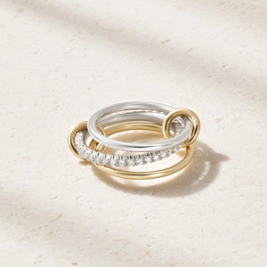 May include: A multi-band ring featuring three interlocking circles. One band is polished yellow gold, one is polished silver-tone metal, and the third is a silver-tone band encrusted with a row of small, clear, sparkling round-cut stones.