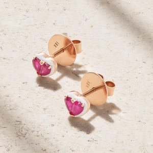 May include: A pair of 18K rose gold stud earrings featuring heart-shaped pink gemstones framed by white enamel borders. The earrings include matching rose gold post backs stamped with 18K, showcasing a polished metal finish and vibrant pink stones.