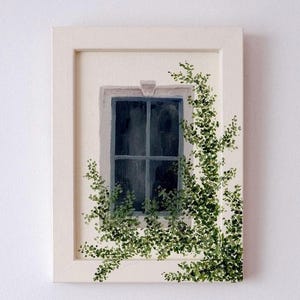 Pode incluir: Uma pintura emoldurada apresentando uma janela retangular com moldura e vidros azul-escuros. Trepadeiras de hera verde com folhas pequenas crescem ao longo da lateral e da parte inferior da janela. A obra está numa moldura de madeira clara.