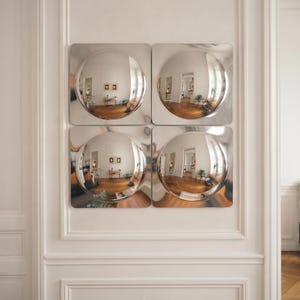Pode incluir: Um conjunto de quatro espelhos de parede quadrados dispostos numa grelha de dois por dois. Cada espelho apresenta uma superfície prateada polida e refletora com um centro côncavo circular profundo que cria um reflexo distorcido da sala.