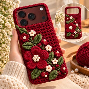 May include: A deep red crochet phone case featuring a textured, hand-stitched floral design. The case is adorned with dark green crocheted leaves, small white flowers, and a large central red flower with a cluster of white pearl-like beads at its centre.