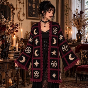 May include: A black crochet cardigan featuring a repeating pattern of beige crescent moons and pentagrams within square motifs. The garment has wide sleeves and is bordered with a scalloped dark red trim along the front opening and hem.