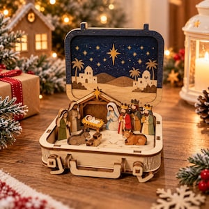 May include: A wooden suitcase-style nativity scene featuring a dark blue night sky backdrop with a large star, palm trees, and buildings. Inside are carved figures of the holy family, three wise men, and animals around a manger.