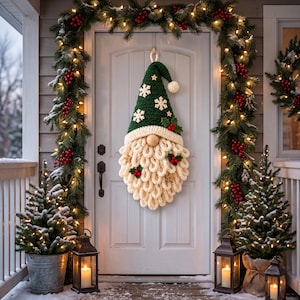 May include: A crochet gnome wall hanging featuring a dark green pointed hat with white snowflake appliques, a cream-colored brim, a round wooden nose, and a long, thick, cream-colored yarn beard accented with small red berries and wooden stars.