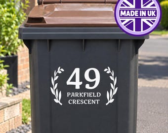 Op de afbeelding: Een donkergrijze buitenafvalbak met een bruin deksel en een witte vinylsticker. De sticker toont het nummer 49 boven de tekst PARKFIELD CRESCENT, geflankeerd door twee witte lauriertakken. Een paarse cirkelvormige badge bevat de tekst MADE IN UK.