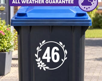 Op de afbeelding: Een donkergrijze afvalcontainer met een blauw deksel voorzien van een witte ronde sticker met het nummer 46, omringd door een blad- en bloemmotief. Een paarse banner bovenaan toont de tekst ALL WEATHER GUARANTEE met een weericoon.