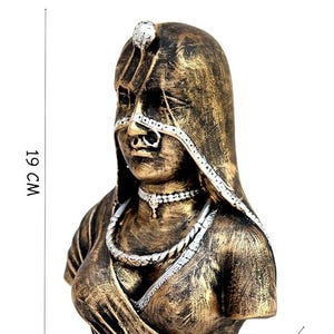 Op de afbeelding: Een bronskleurig borstbeeld van een persoon met een hoofdbedekking en sieraden, waaronder een neusring en een ketting. De sculptuur heeft zilverkleurige accenten op het hoofddeksel en de sieraden. Het is 19 cm hoog, 14 cm breed en 8 cm diep.