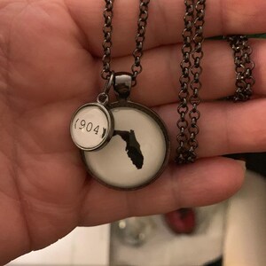 May include: A necklace with a dark chain and pendant. The pendant features a white background with a black silhouette of Florida. A smaller charm displays the number "904".