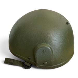 Può includere: Un elmetto da combattimento verde oliva con una finitura esterna testurizzata. L'elmetto presenta una forma a cupola arrotondata, un piccolo perno sporgente sulla parte superiore e una staffa di montaggio laterale fissata con rivetti. Cinturino in tessuto.
