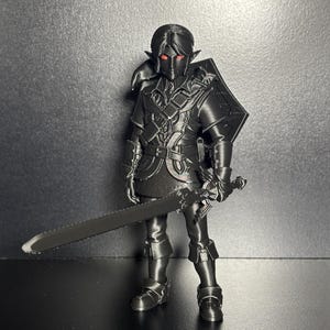 May include: A black 3D printed figurine of a warrior character with pointed ears, wearing detailed armour and a tunic. The figure features bright red eyes and holds a long sword in one hand, with a shield strapped to the back, standing in a pose.