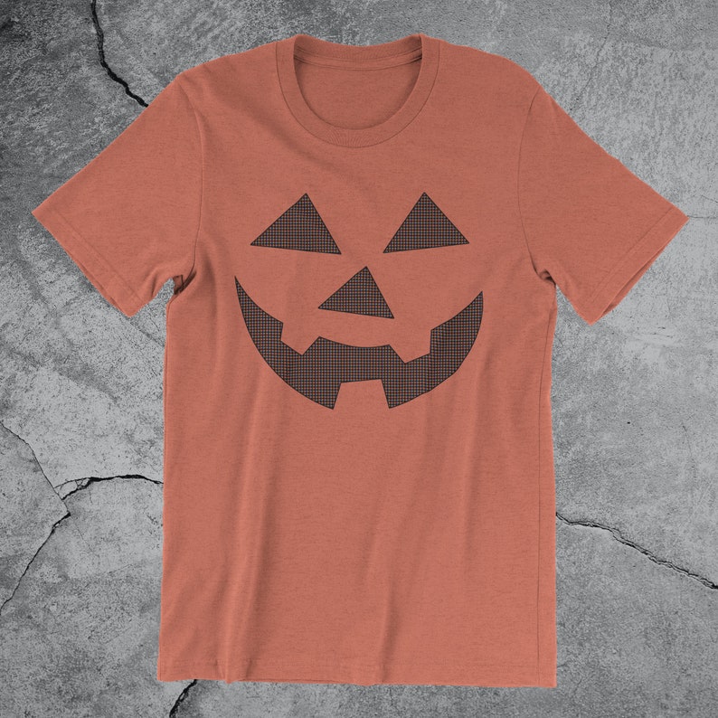 Może przedstawiać: Pomarańczowy t-shirt z nadrukiem czarno-białej kratkowanej twarzy jack-o'-lantern.