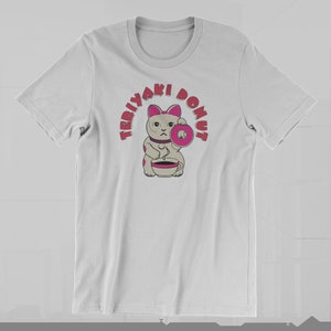 May include: White t-shirt featuring a cartoon cat holding a pink donut and a cup. The text "TERIYAKI DONUT" arches above the cat in pink letters. The cat has pink ears and spots, and a serious expression.