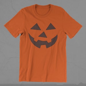 Może przedstawiać: Pomarańczowa koszulka z nadrukiem czarno-białej kratkowanej twarzy jack-o'-lantern.