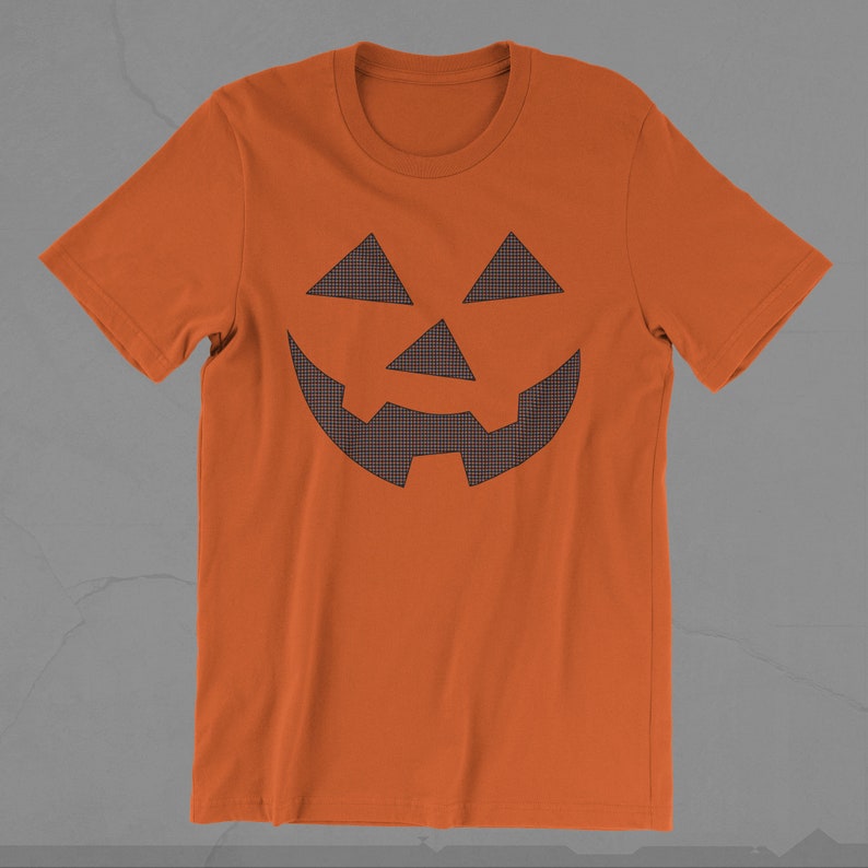 Może przedstawiać: Pomarańczowa koszulka z nadrukiem czarno-białej kratkowanej twarzy jack-o'-lantern.
