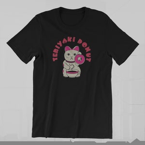 May include: Black t-shirt featuring a cartoon cat holding a donut and a cup of coffee. The text "TERIYAKI DONUT" is printed above the cat in a pink, circular design. The cat has gray fur and pink accents.
