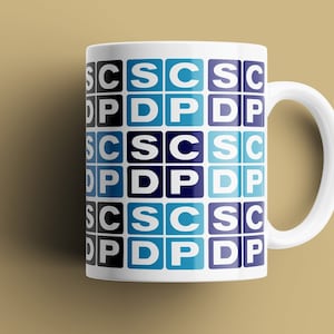 May include: White ceramic mug with a repeating pattern of blue and white squares. Each square contains the letters "CSC" or "PDP" in a sans-serif font. The mug has a curved handle and is set against a tan background.