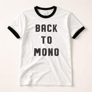 Puede incluir: Camiseta blanca con ribetes negros en el cuello y las mangas. La camiseta presenta el texto "BACK TO MONO" en letras negras y en negrita. La camiseta está hecha de un material suave y cómodo.