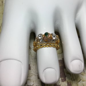 Puede incluir: Anillo de dedo del pie de oro y plata con piedras transparentes y rosas y un acento de piedra verde.