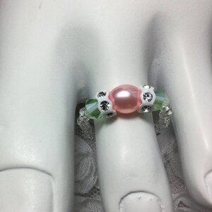 Puede incluir: Un anillo de dedo del pie de cuentas rosa y verde con una sola perla rosa en el centro.