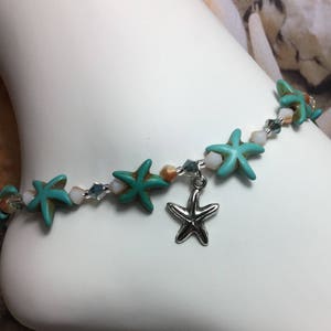 Op de afbeelding: Een turquoise en witte kralen enkelband met een zilveren zeester-bedel. De enkelband heeft turquoise zeester kralen, witte schelp kralen en heldere kristallen kralen.