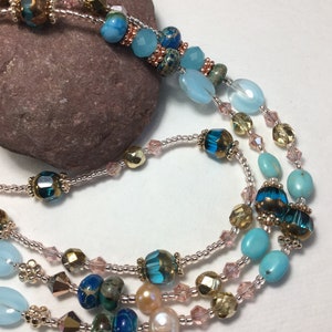 May include: A multi-strand necklace with turquoise, blue, and gold beads. The necklace is made with a variety of materials, including glass, metal, and stone.