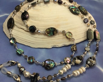 May include: A beaded eyeglass chain with abalone shell and pearl accents. The chain is silver and features a variety of iridescent colors.