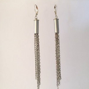 May include: A pair of silver dangle earrings with a cylindrical charm and multiple chain strands hanging from each charm.