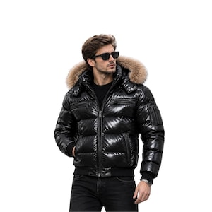 May include: A glossy black puffer jacket featuring a high collar, a front zip fastening, and a detachable hood trimmed with thick, light brown faux fur. The jacket includes horizontal quilted panels, zipped chest pockets, and ribbed cuffs.