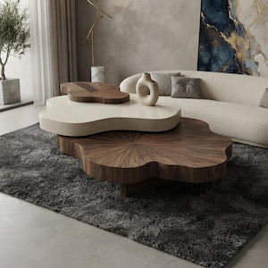 May include: A multi-tiered coffee table featuring a large, dark wood base with a radial grain pattern and a smaller, cream-colored top tier with an organic, cloud-like shape. A small, dark wood accent piece and a smooth, cream-colored ceramic vase sit on top.