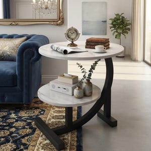 May include: A two-tier side table with a white faux marble top and shelf, supported by a curved black metal frame. The table features a circular design with a sturdy base, providing two levels for storage and display in a living room setting.