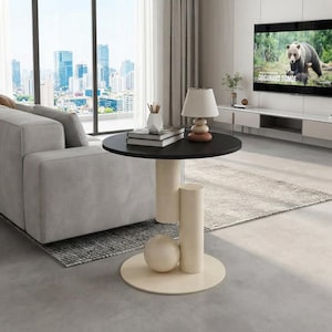 Peut inclure: Une table d'appoint ronde noire avec une base crème composée d'une grande sphère et de deux supports cylindriques. La table porte une pile de livres et une petite lampe à abat-jour crème. Le design est géométrique avec des surfaces lisses.