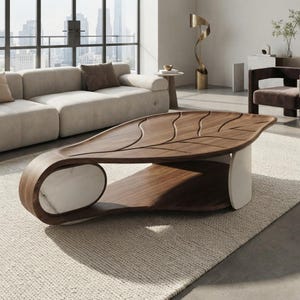 Peut inclure: Une table basse avec un plateau en bois foncé sculpté d'un motif de nervures en forme de feuille. La base est composée d'éléments en bois foncé courbé et en pierre blanche lisse, formant une silhouette fluide et continue au sol.