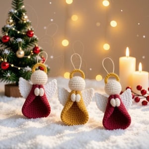 May include: Three handmade crochet angel ornaments featuring cream-colored heads, white wings, and gold halos. Two angels wear deep red robes, while the center angel wears a mustard yellow robe. Each ornament includes a small loop for hanging.