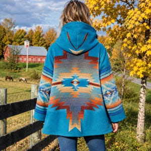 May include: A hooded jacket in a vibrant turquoise blue featuring a large, symmetrical geometric pattern on the back. The design incorporates horizontal bands of orange, brown, and dark blue, creating a bold, multi-colored motif.
