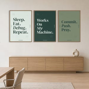 May include: Three rectangular wall posters in thin wooden frames. The left poster is light gray with the text "Sleep. Eat. Debug. Repeat." The middle poster is dark green with "Works On My Machine." The right poster is sage green with "Commit. Push. Pray."