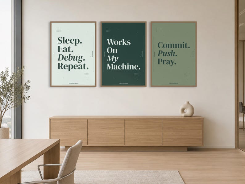 May include: Three rectangular wall posters in thin wooden frames. The left poster is light gray with the text "Sleep. Eat. Debug. Repeat." The middle poster is dark green with "Works On My Machine." The right poster is sage green with "Commit. Push. Pray."