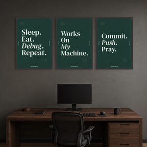 May include: Three dark green rectangular wall posters with white text. The first reads Sleep. Eat. Debug. Repeat. The second reads Works On My Machine. The third reads Commit. Push. Pray. Each poster features small geometric grid patterns in the corners.