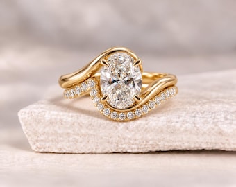 Pode incluir: Um anel de ouro amarelo com uma pedra preciosa central transparente de corte oval fixada por quatro garras. A banda tem um design curvo e assimétrico com uma fila de pequenas pedras transparentes cravadas em pavé.