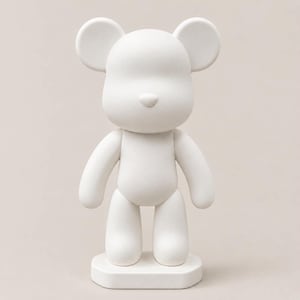 May include: A matte white bear-shaped figurine standing on a rectangular base. The figure features a smooth, rounded head with prominent circular ears, a small nose, and a simple, featureless face. The body has rounded limbs and a solid torso.