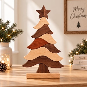 Peut inclure: Une sculpture de sapin de Noël décorative composée de segments de bois ondulés empilés, alternant des tons clairs et foncés. L'arbre est surmonté d'une étoile et repose sur une base rectangulaire, révélant les veines naturelles du bois.