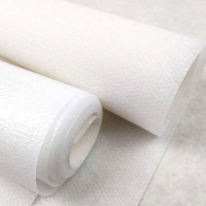 Può includere: Due rotoli di carta bianca, semitraslucida e testurizzata. La superficie della carta presenta una grana fine, fibrosa e leggermente irregolare, apparendo leggera e delicata. I rotoli sono posizionati fianco a fianco, mostrando gli strati.