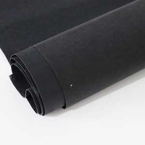 Peut inclure: Un rouleau de tissu noir uni avec une finition mate. Le textile est partiellement déroulé, révélant une texture de surface lisse et cohérente sur toute la longueur du matériau. Le tissu est opaque et présente une couleur noire uniforme.