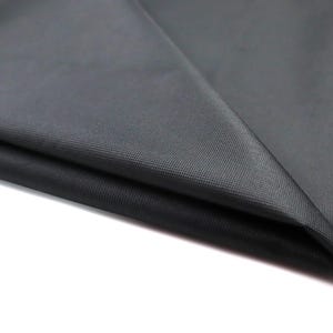 May include: A solid black fabric pouch featuring a fine, woven texture. The pouch is folded over at the top, revealing a smooth, consistent matte black surface. The material appears durable and opaque, with a clean, simple construction throughout.
