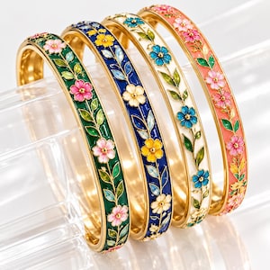 Può includere: Quattro bracciali rigidi in metallo dorato con motivi floreali in smalto. I bracciali sono disponibili in verde, blu scuro, bianco e corallo, ciascuno decorato con fiori colorati e foglie verdi disposti in un motivo a tralcio sulla fascia.