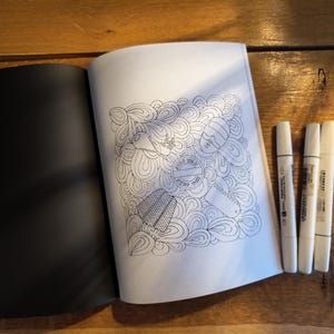 May include: An open coloring book with a black page on the left and a white page on the right featuring a line art illustration of abstract swirls and various objects, accompanied by three white markers with black text on their barrels.