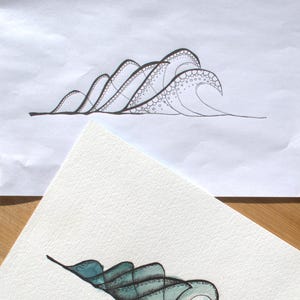 May include: A black ink line drawing of ocean waves on white paper featuring intricate circular patterns and stippling details, accompanied by a partially visible watercolor painting of waves in shades of teal and blue with three black pens.